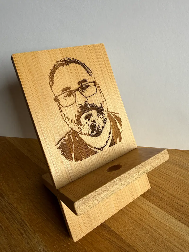 Support de téléphone en bambou gravé au laser avec un portrait d'homme, vue de trois-quarts posée sur une table